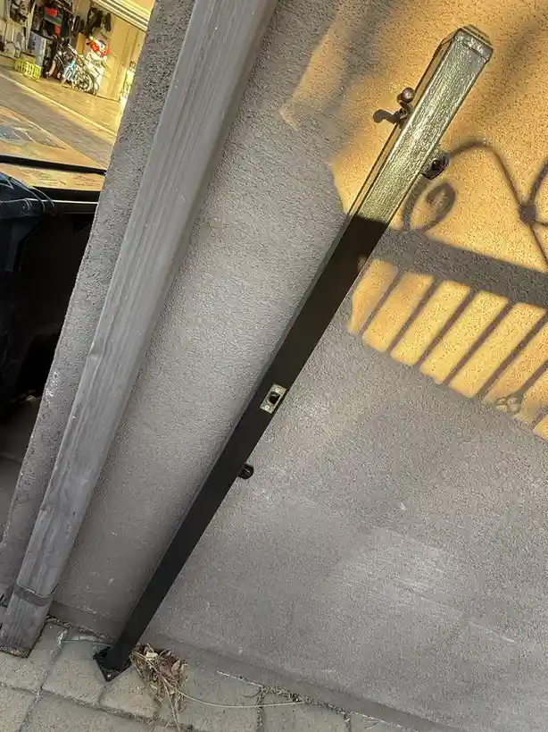 A close-up photo shows a black metal parking meter pole leaning against a textured gray wall, casting a shadow that…