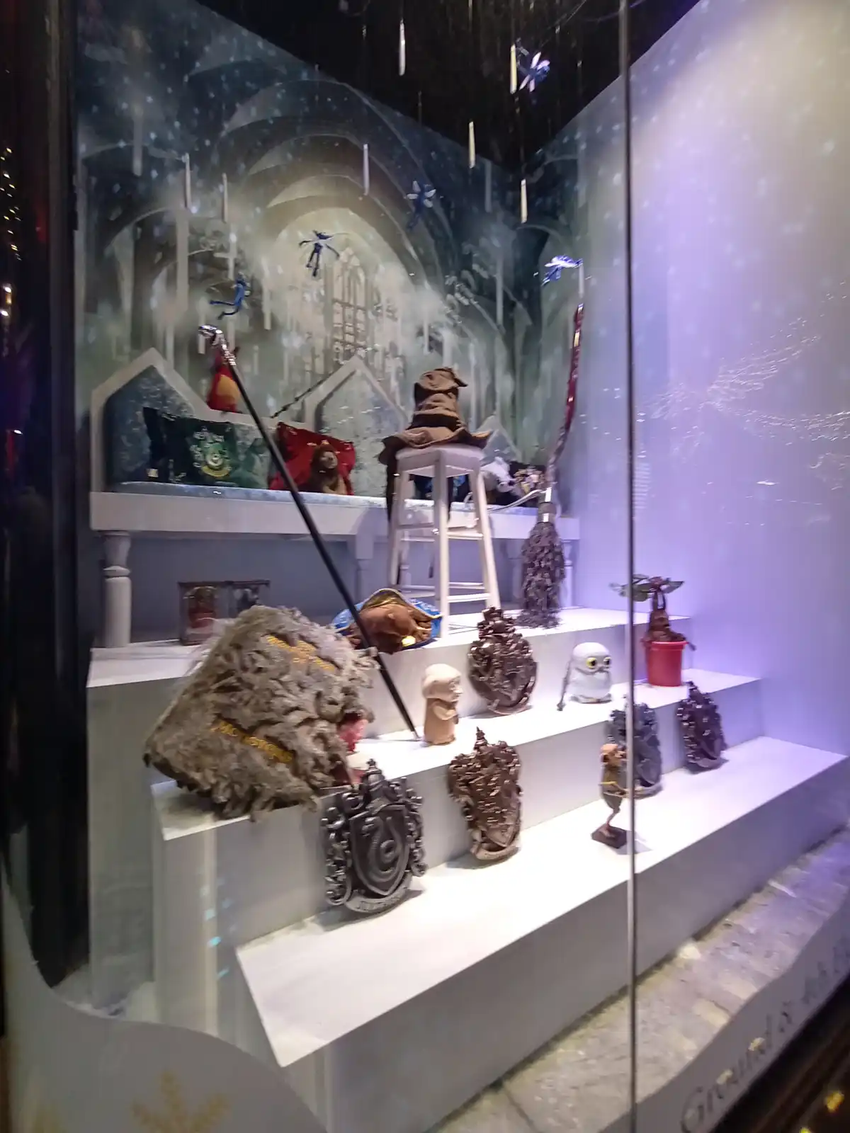 A Harry Potter-themed store window display features a Sorting Hat on a stool, wands, house banners, and various figurines…