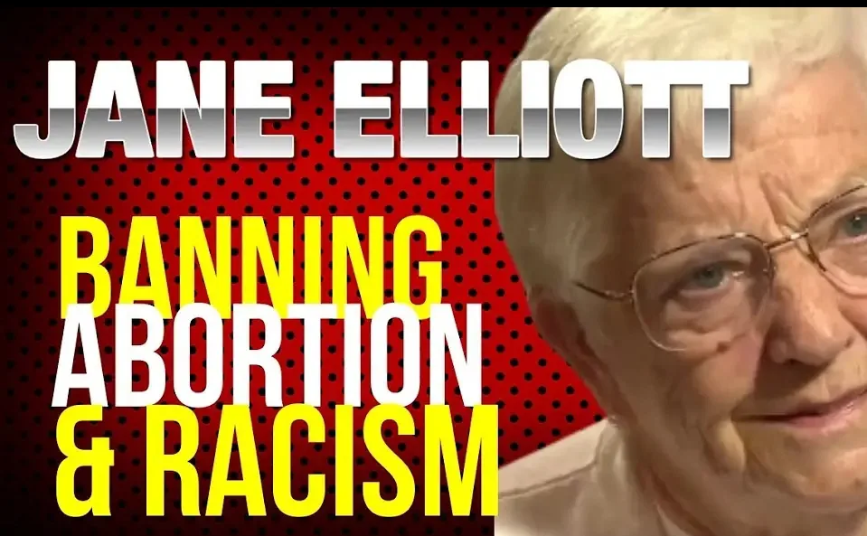 An image of Jane Elliott, an elderly woman with white hair and glasses, is overlaid with bold text. The text reads 'JANE…