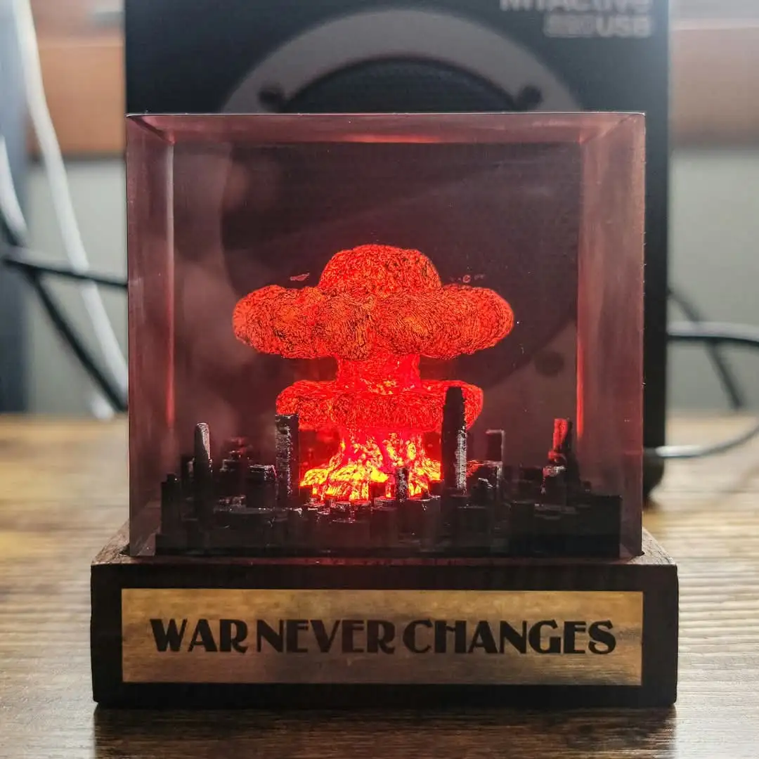 A small, illuminated diorama in a clear cube shows a glowing red nuclear mushroom cloud exploding over a miniature cityscape…