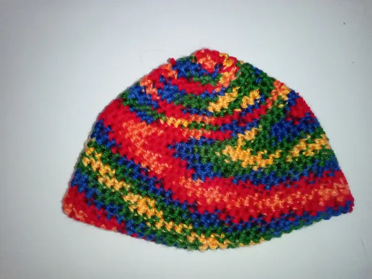 a close-up photo of a hand-knitted or crocheted hat with a vibrant, swirling pattern of red, blue, green, and yellow yarn…