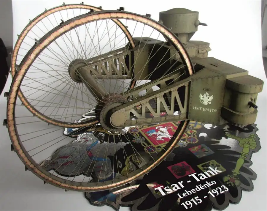 A model of a large, olive-drab, early 20th-century armored vehicle with massive spoked wheels and a turret, labeled…