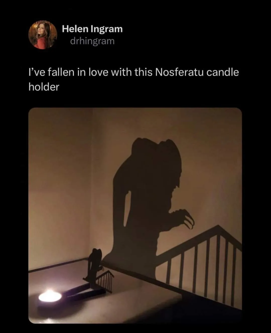 A small candle holder shaped like a vampire is lit, casting a large, menacing shadow of Nosferatu on the wall behind it…