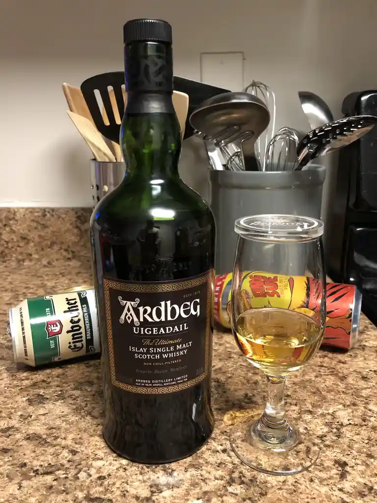 A bottle of Ardbeg Uigeadail Islay Single Malt Scotch Whisky sits on a kitchen counter next to a partially filled whisky…