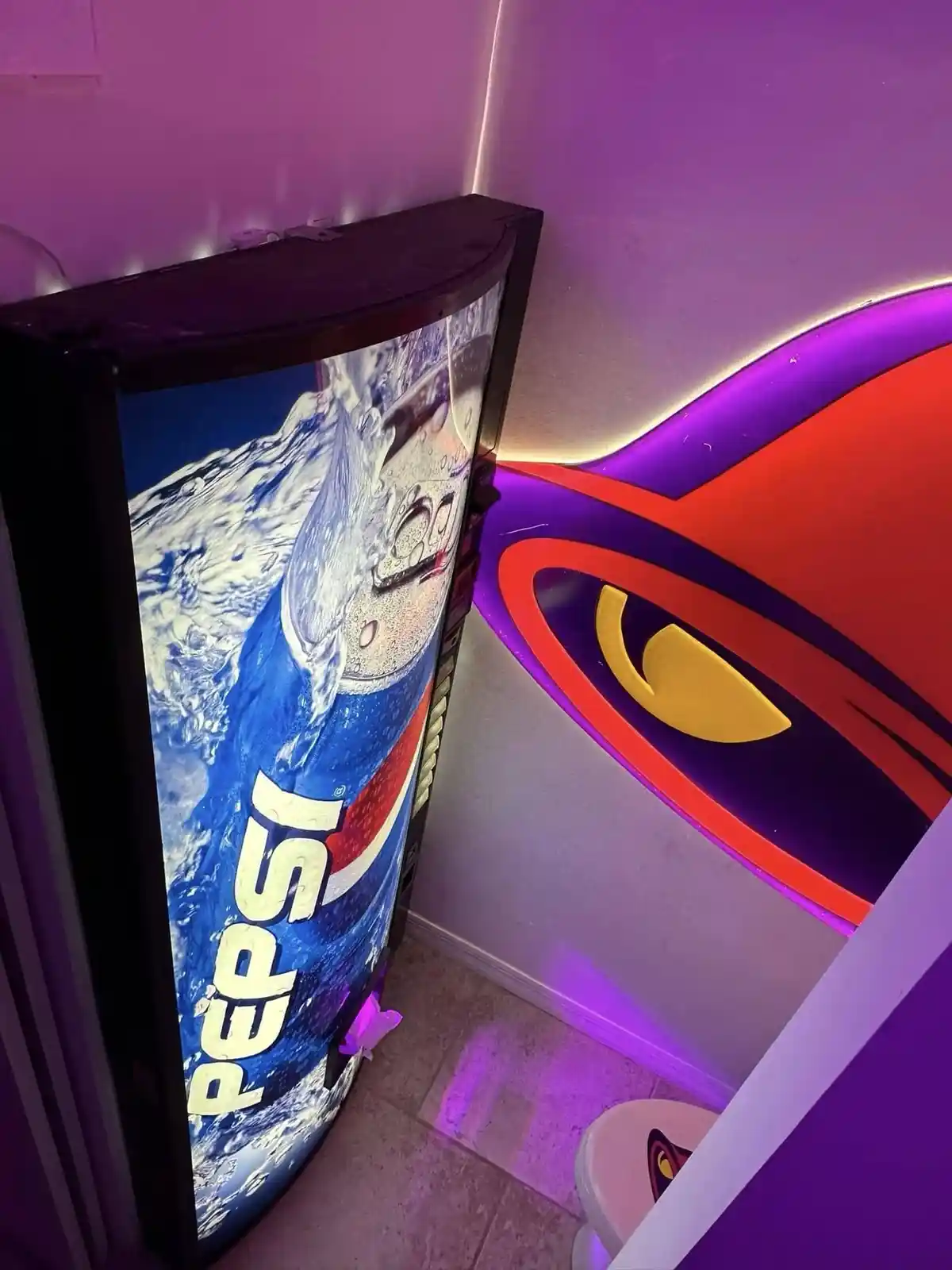 A curved Pepsi vending machine with a splash graphic is positioned next to a large, stylized eye logo with a yellow iris…
