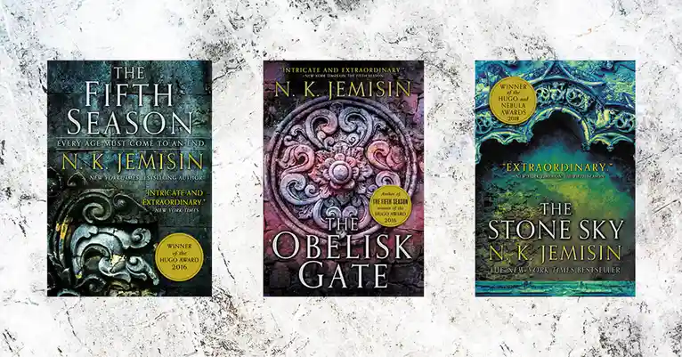 Three book covers of N.K. Jemisin's 'Broken Earth' trilogy are displayed side-by-side on a marble background. The left cover…
