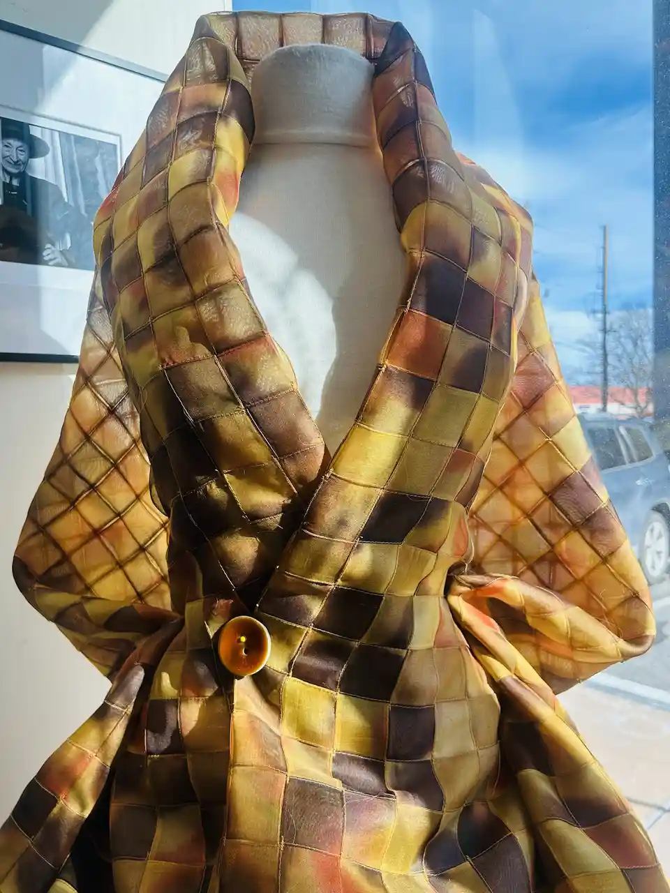 A close-up photo shows a mannequin wearing a luxurious, quilted coat with a patchwork pattern of gold, brown, and orange…