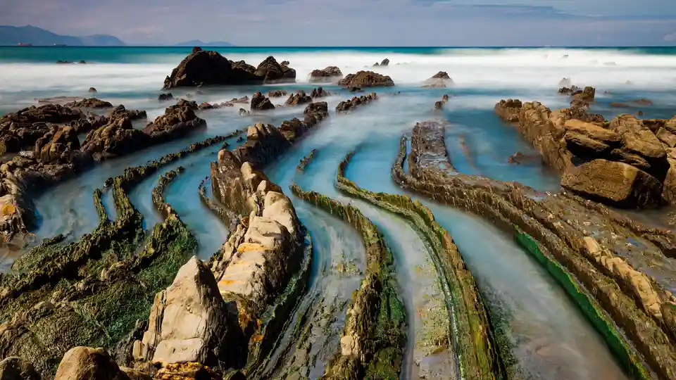 Rugged, layered formations resembling lasagna emerge from the northern Spain coast, revealed by the tide's withdrawal. These…