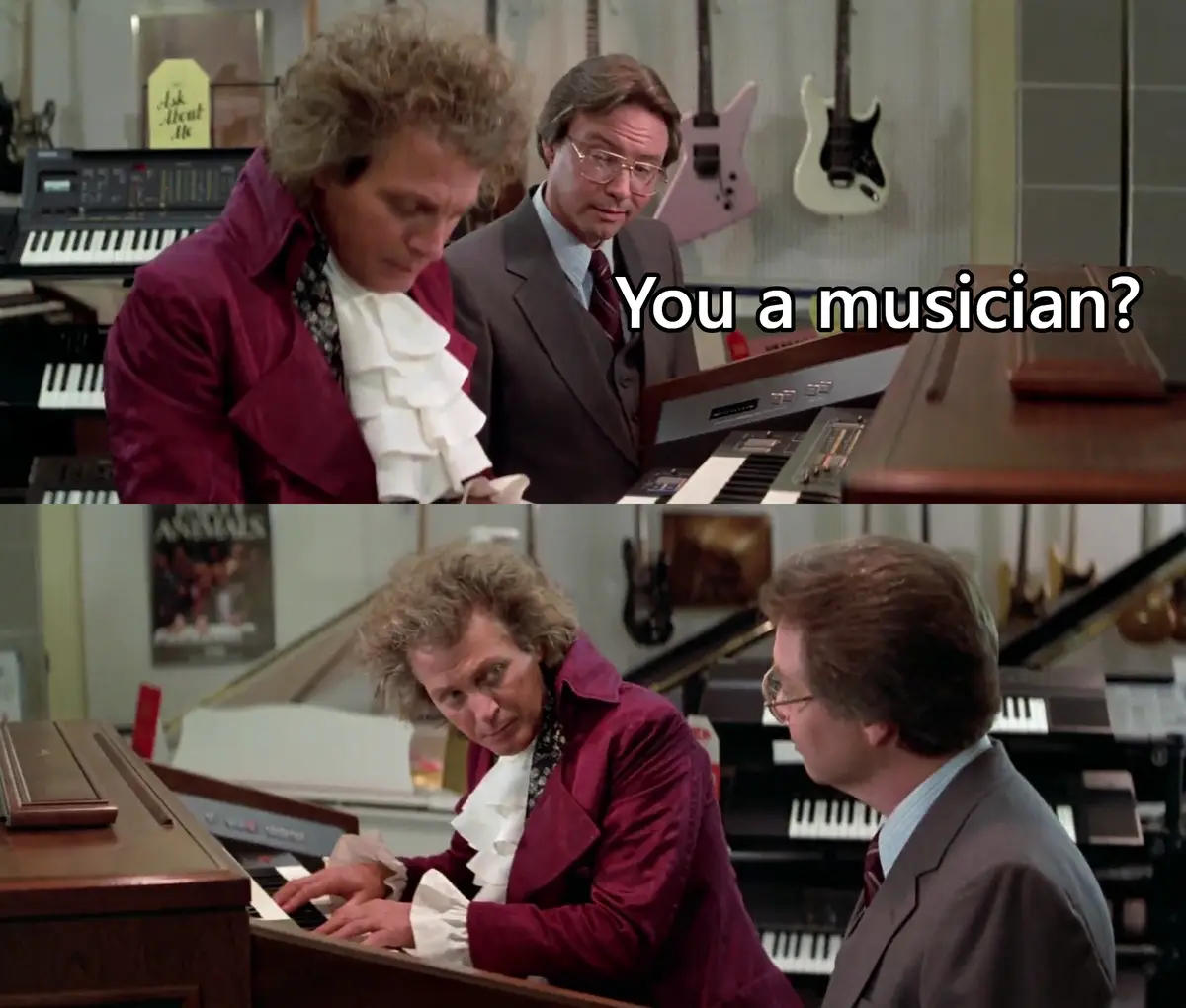 Two men are in a music store with keyboards and guitars in the background. The man in the maroon jacket and white ruffled…