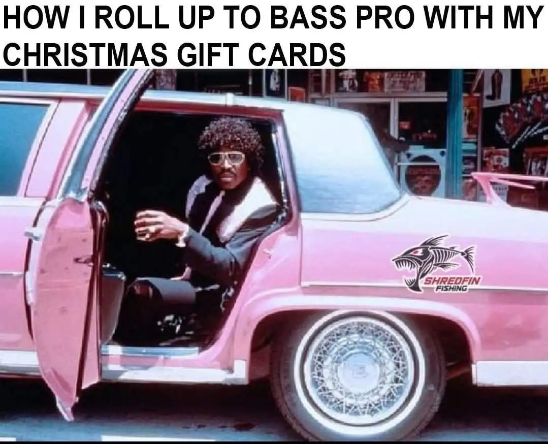 A man with an afro and glasses sits in the driver's seat of a pink station wagon with the door open, looking out. The car…