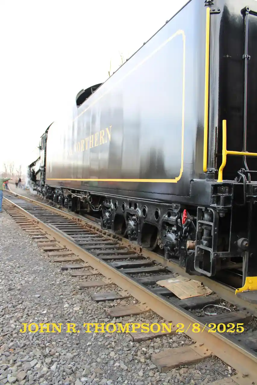 A low-angle photo shows the side of a black steam locomotive with gold trim and 'NORTHERN' lettering, moving on tracks with…