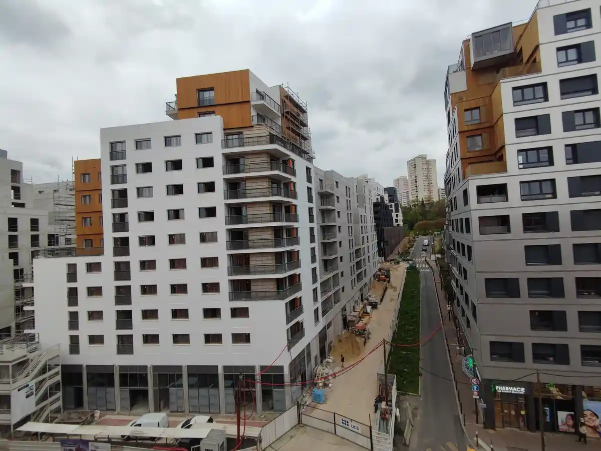 A high-angle photo of modern apartment buildings under construction in a city, with scaffolding visible on some structures…