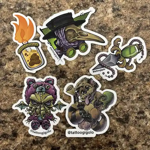 Five colorful, cartoonish stickers with a steampunk and fantasy theme are arranged on a brown speckled countertop. One shows…