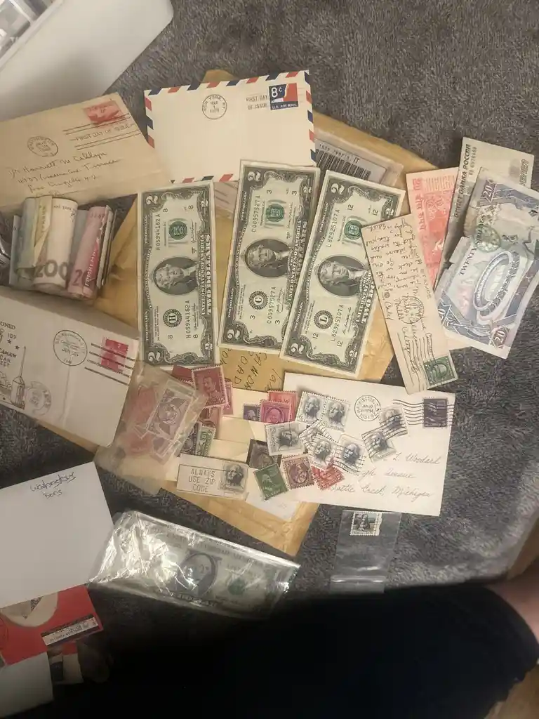 An overhead shot displays a collection of vintage U.S. and foreign currency, old postage stamps, and envelopes scattered on…