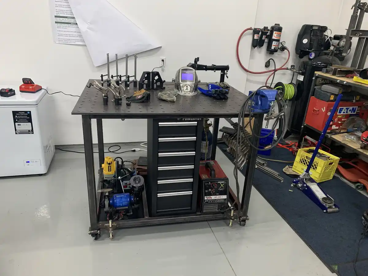 A well-organized welding station in a garage, featuring a metal workbench with a Miller welding helmet, gloves, clamps, and…