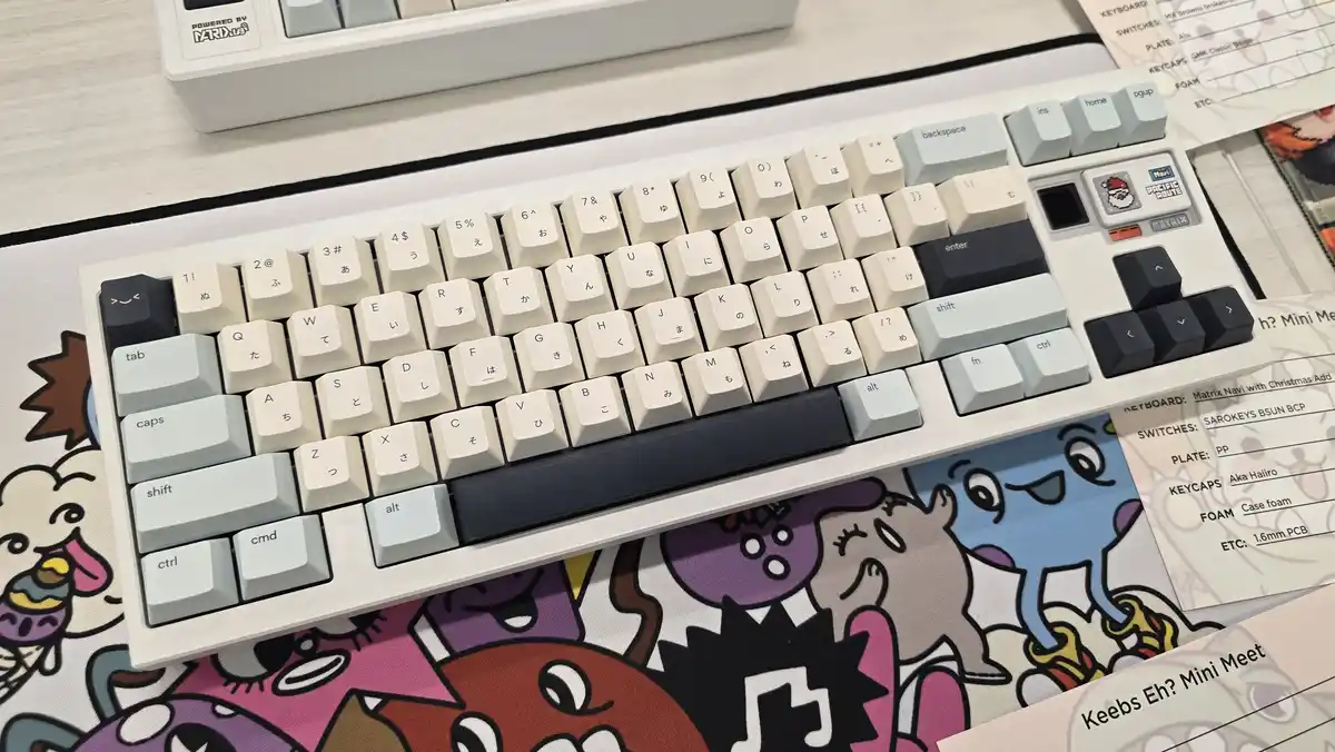 A close-up photo of a white mechanical keyboard with beige and black keys, featuring Japanese characters and symbols on the…
