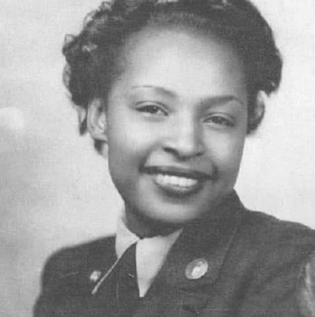 A black-and-white portrait of a smiling Black woman in a military-style uniform with a collar and tie. The image has…