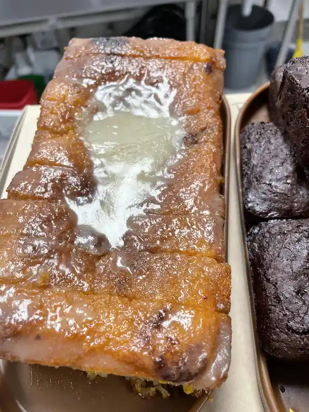A close-up photo shows a rectangular, golden-brown cake with a glossy, caramelized top and a large, melted white substance…