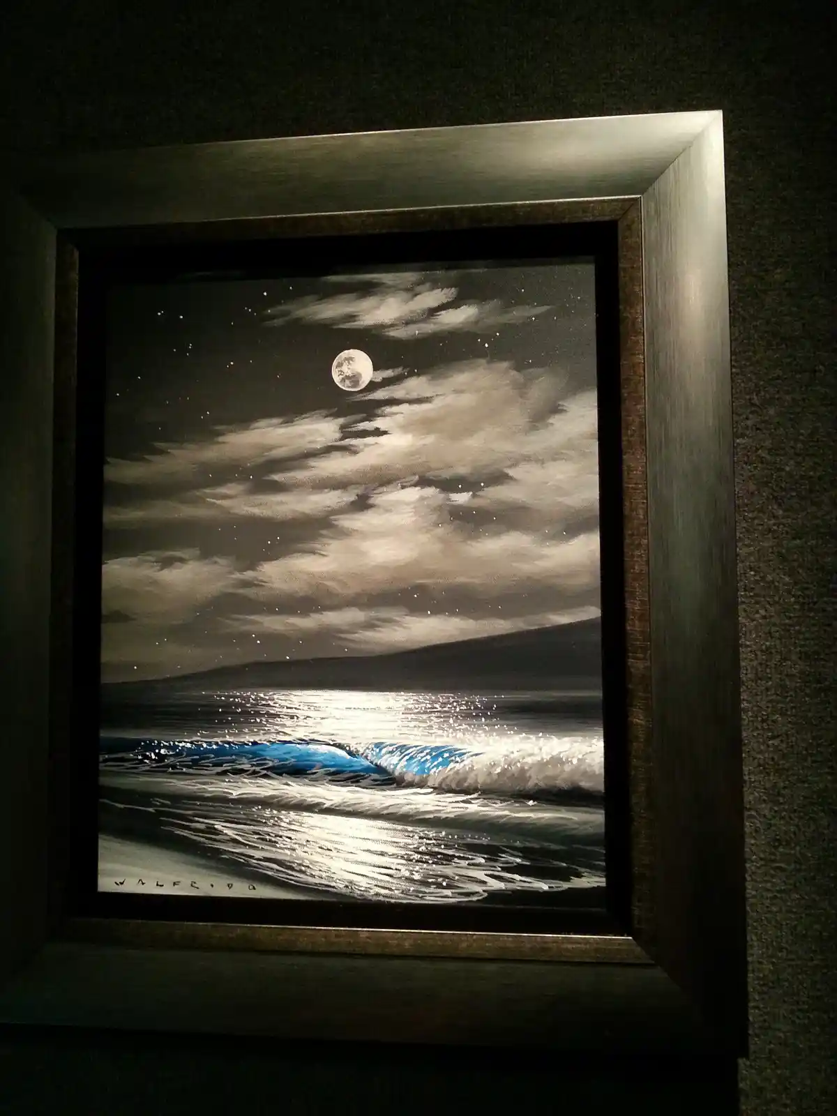 A framed painting depicts a serene night scene with a full moon, stars, and clouds over a body of water. The moon's…