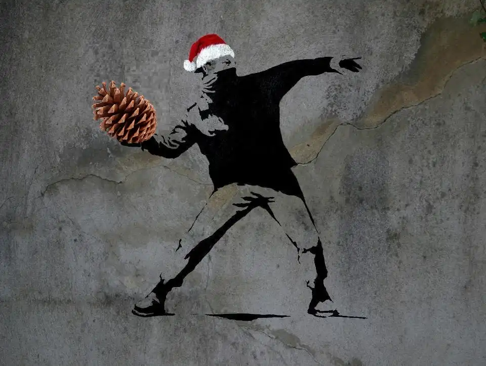 A black stencil graffiti of a person in a red and white Santa hat, mid-throw, holding a large pinecone in their right hand…