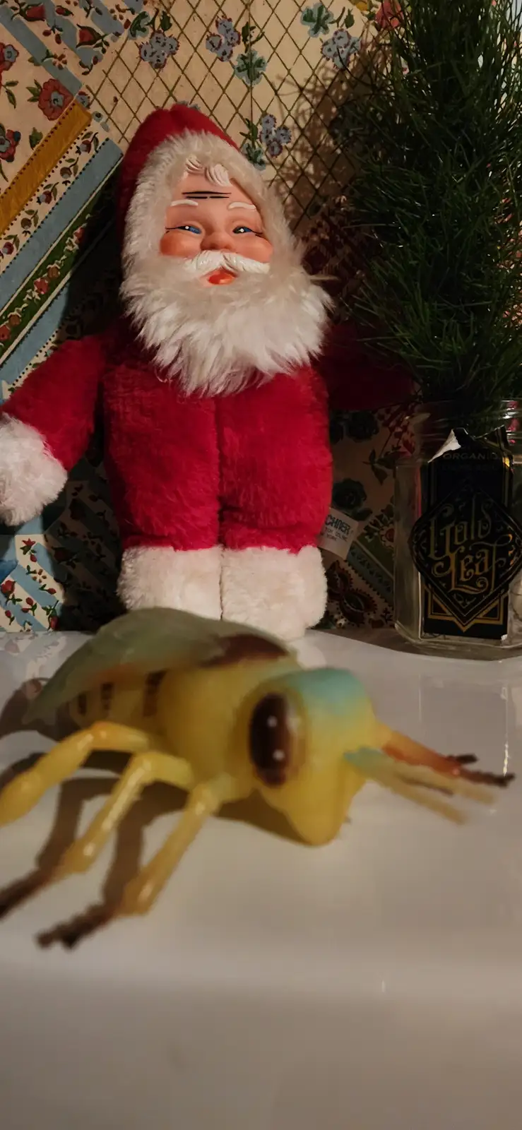 A vintage-style plush Santa Claus doll with a red suit and white beard stands behind a large, yellow plastic bee toy on a…