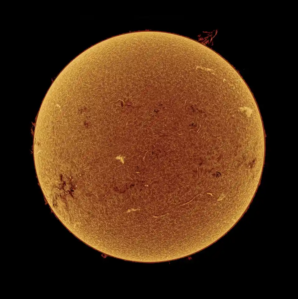 A high-resolution image of the sun's surface, showing its textured, golden-orange photosphere with visible sunspots and…