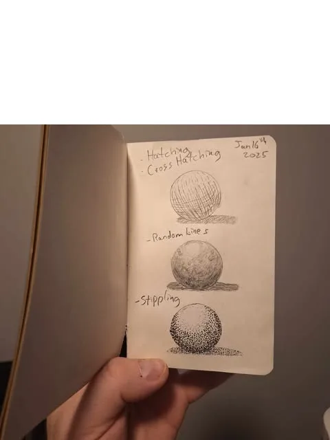 A hand holds an open sketchbook showing three hand-drawn spheres, each labeled with a different shading technique…