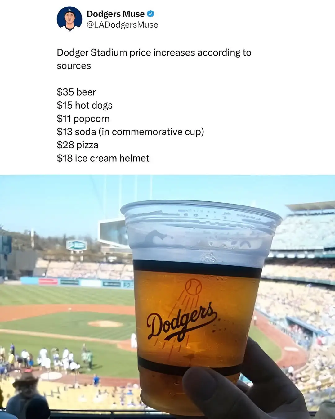 A hand holds a Dodgers-branded plastic cup filled with beer, overlooking a baseball stadium with a field and stands in the…