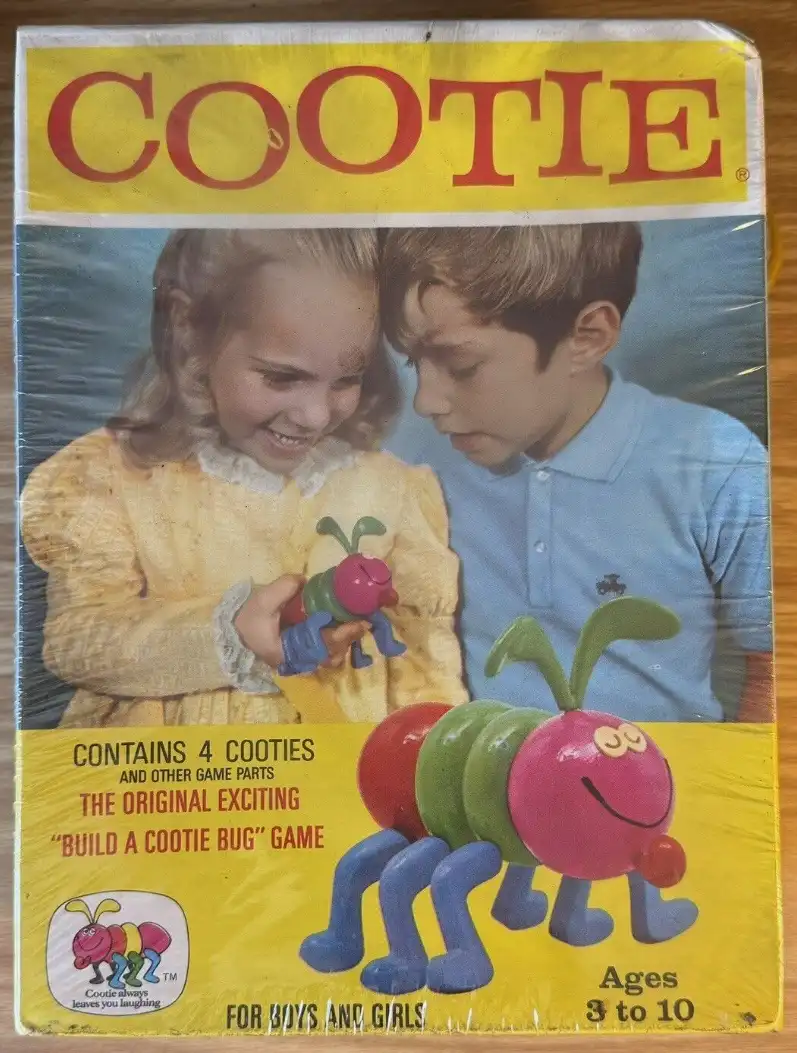 The image shows a vintage toy box for the game 'Cootie,' featuring a smiling girl in a yellow dress holding a small…