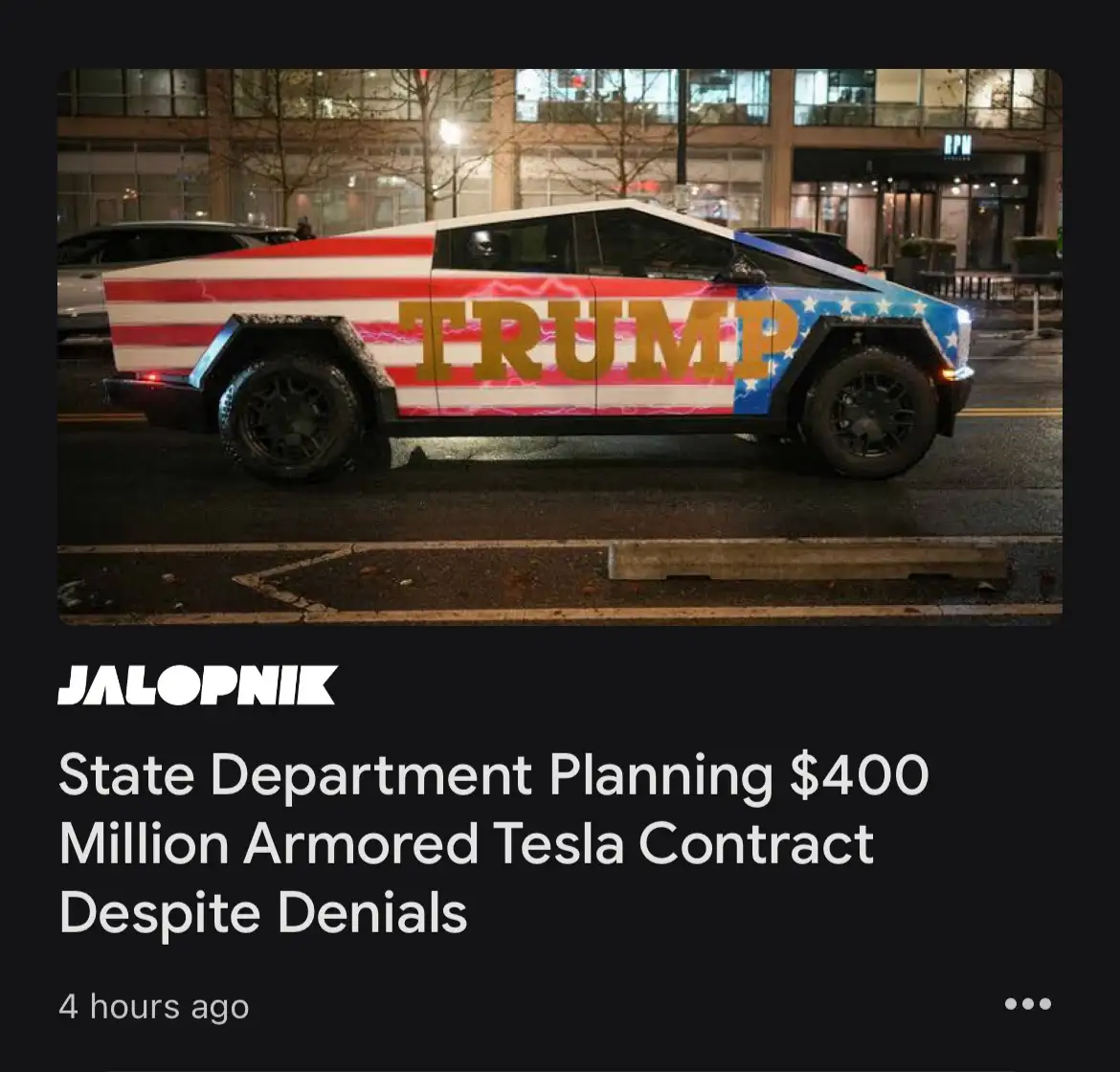 A Tesla Cybertruck is parked on a city street at night, wrapped in a patriotic American flag design with the word 'TRUMP' in…