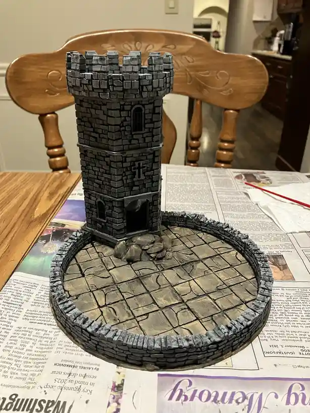 A small, intricately crafted castle model made of what appears to be painted cake sits on a table covered with newspaper…
