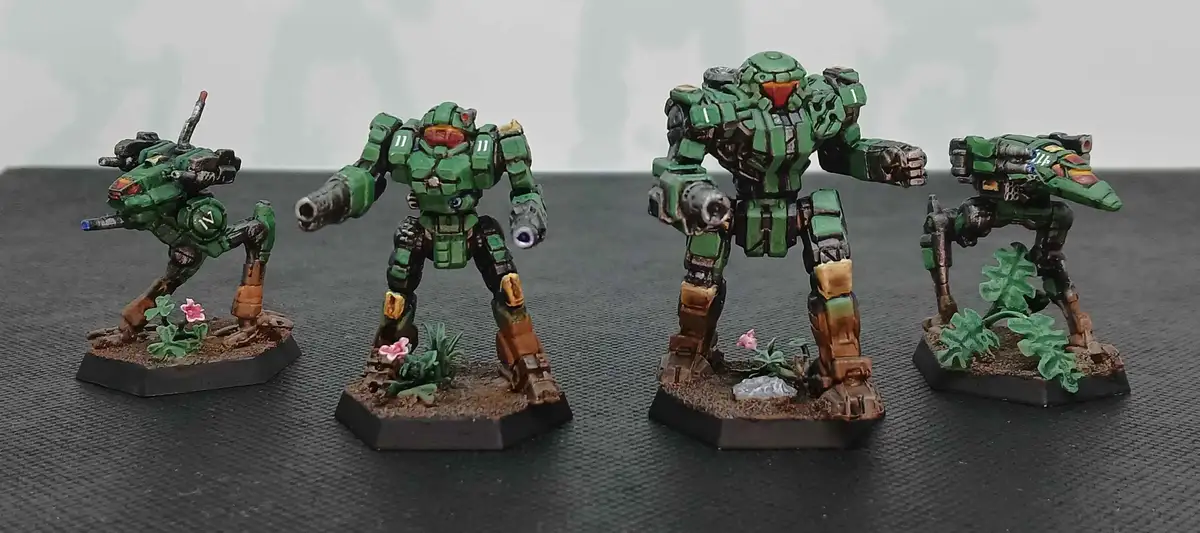 Four green-painted Halo Spartan armor miniatures stand on hexagonal bases with small plants, arranged in a row on a dark…