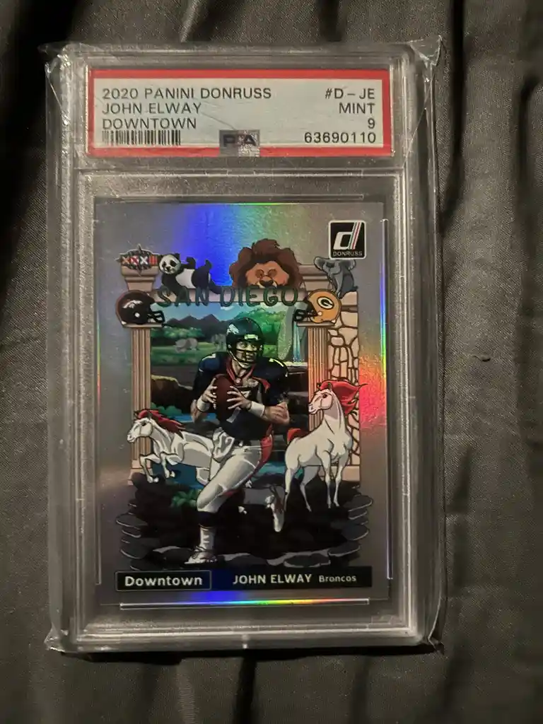 A 2020 Panini Donruss John Elway Downtown football trading card, graded Mint 9 by PSA, is shown in its protective slab. The…