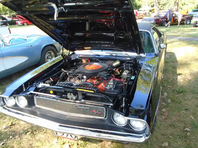 A black 1970 Dodge Challenger RT with its hood open, revealing a red engine and chrome details, parked at a car show with…