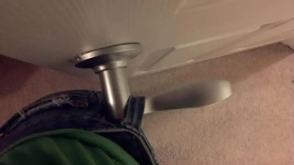 A low-angle shot shows a person's denim-clad hip and green shirt pressing against a silver door handle, seemingly stuck to…