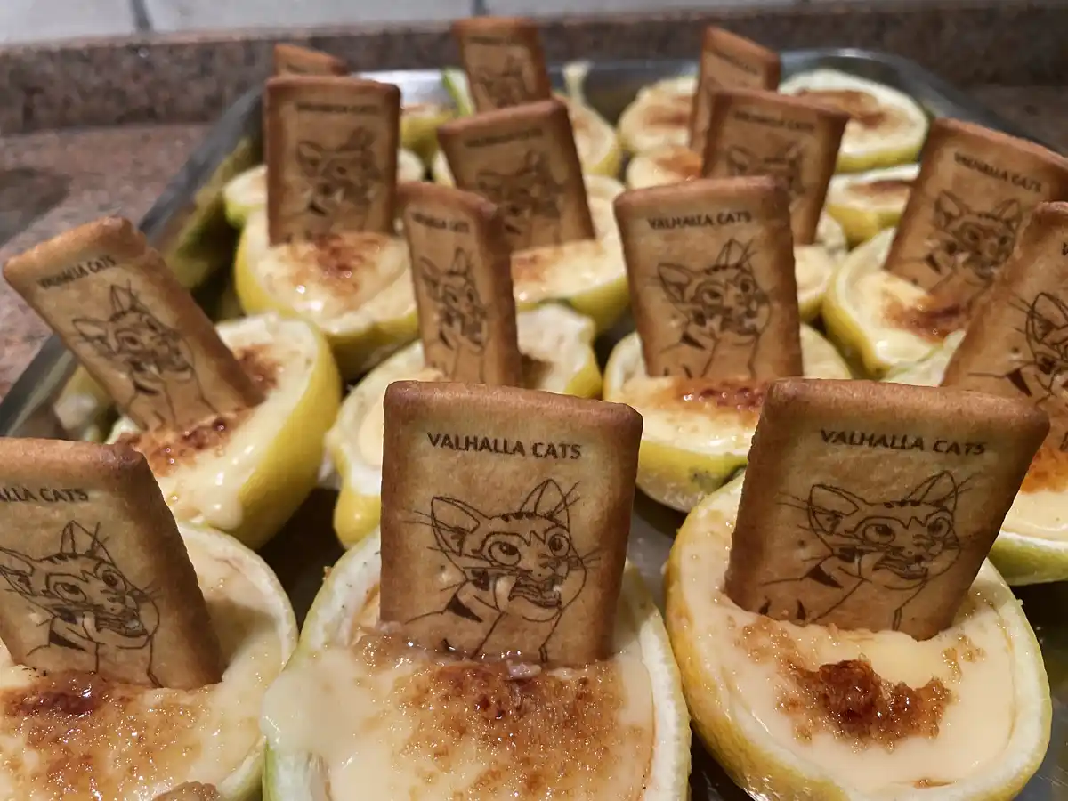 A tray of baked lemon halves filled with a creamy custard and topped with small rectangular crackers. Each cracker has a…
