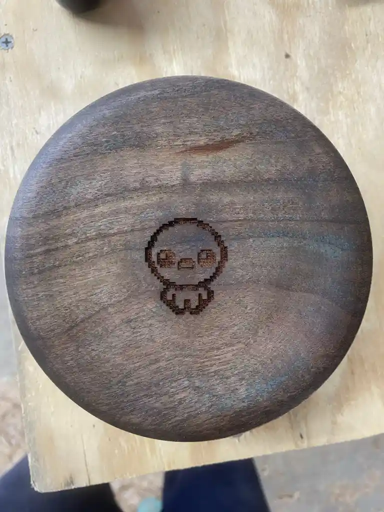 A top-down view of a dark-stained wooden bowl resting on a light-colored wooden surface. The center of the bowl features a…