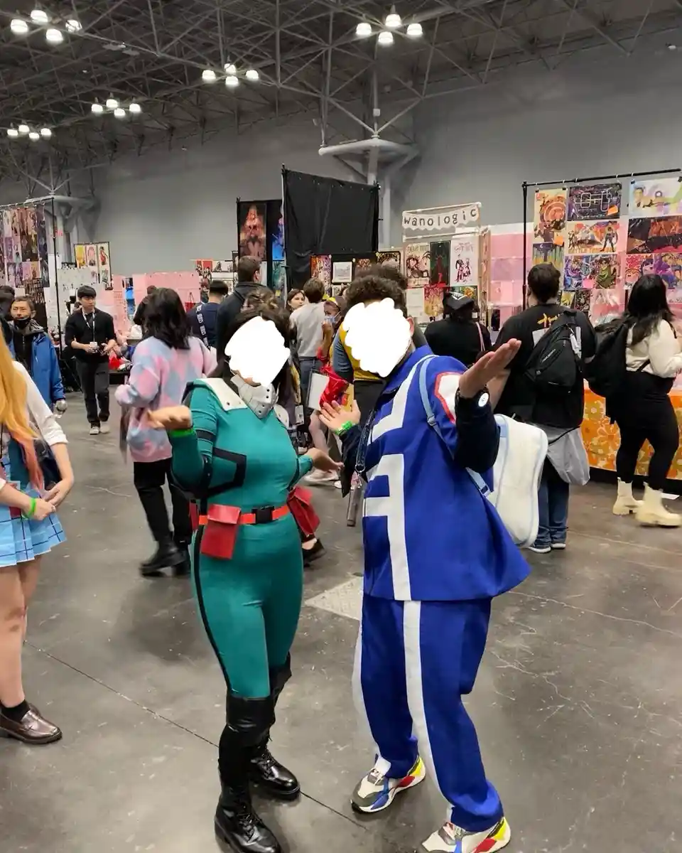 Two cosplayers at a convention, one in a teal and black suit with red belt and boots, the other in a blue and white…