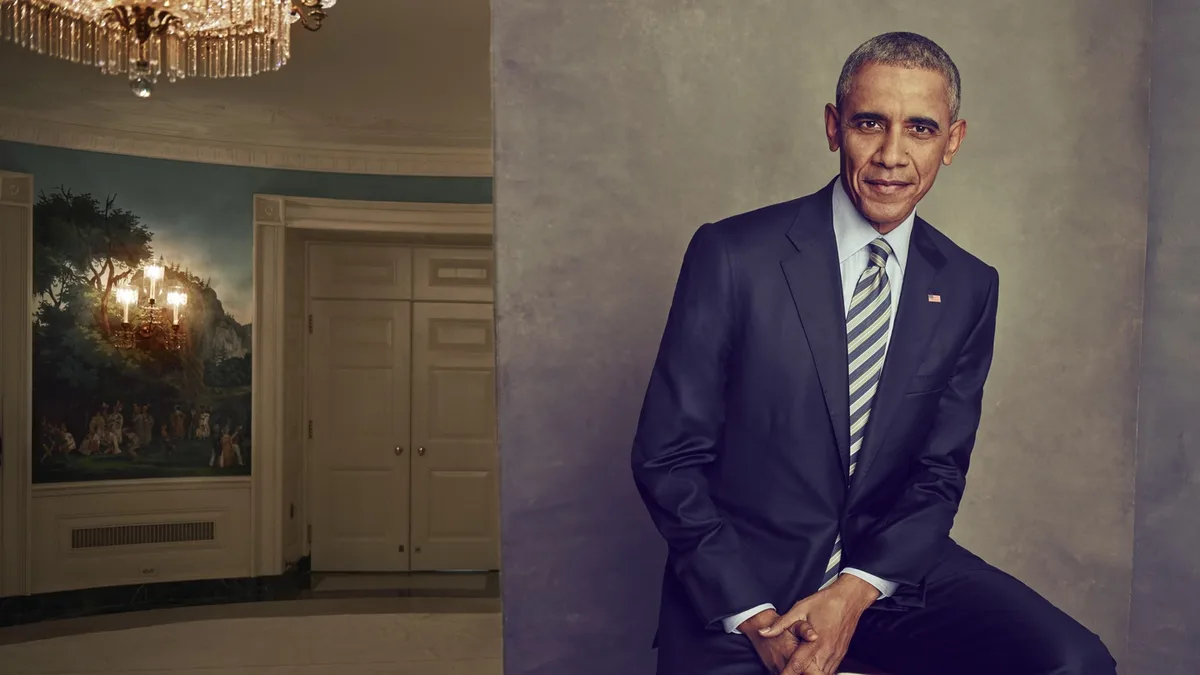 A formal portrait of former president Barack Obama sitting in a suit with a striped tie, next to a doorway revealing a mural…