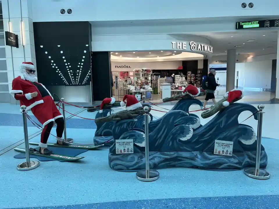 A life-sized Santa Claus statue wearing sunglasses and standing on skis is positioned next to a decorative wave sculpture…