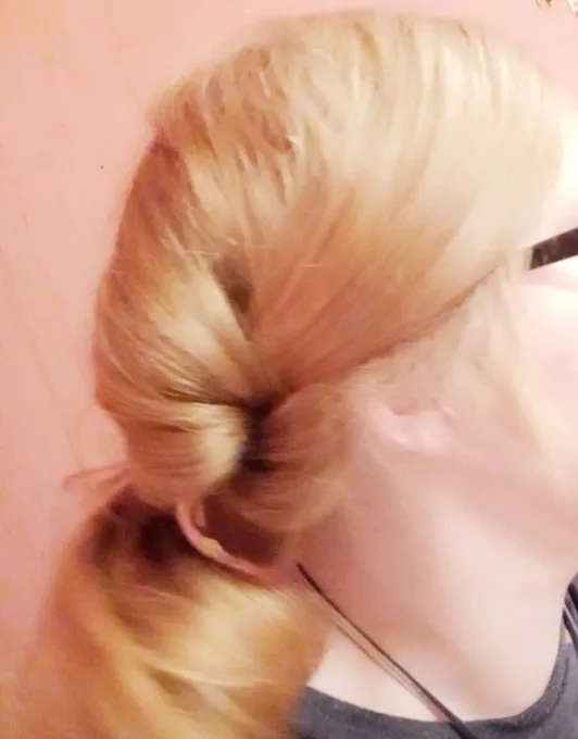 A blurry, close-up photo of a person's blonde hair tied in a messy bun, showing the back of their head and neck against a…