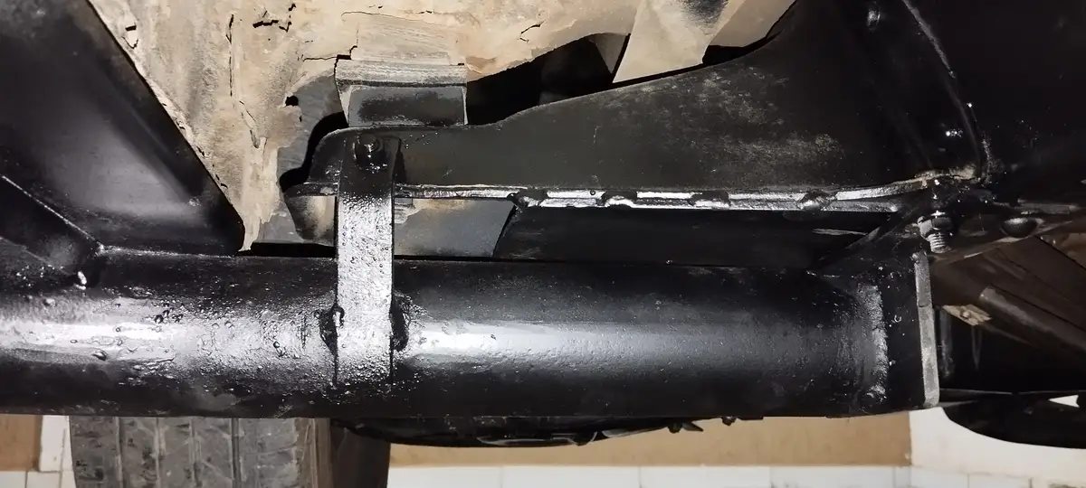 A close-up photo shows the underside of a vehicle, focusing on a black metal exhaust pipe and surrounding frame. A visible…