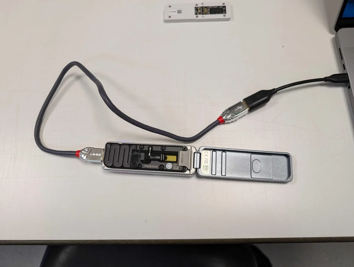 A silver, open USB device with exposed internal components and two USB cables plugged into it, one connected to a laptop on…