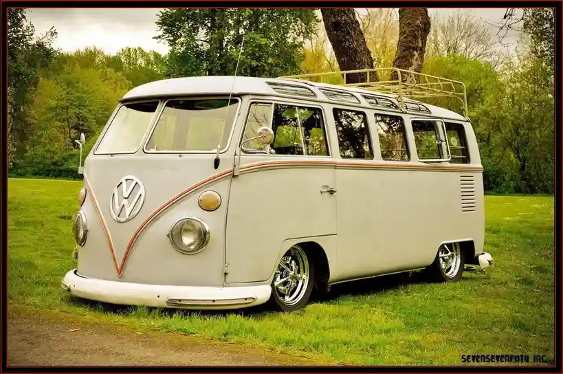 A vintage white Volkswagen Type 2 van with a roof rack is parked on grass near trees. The overlaid text reads 'i'm not a…