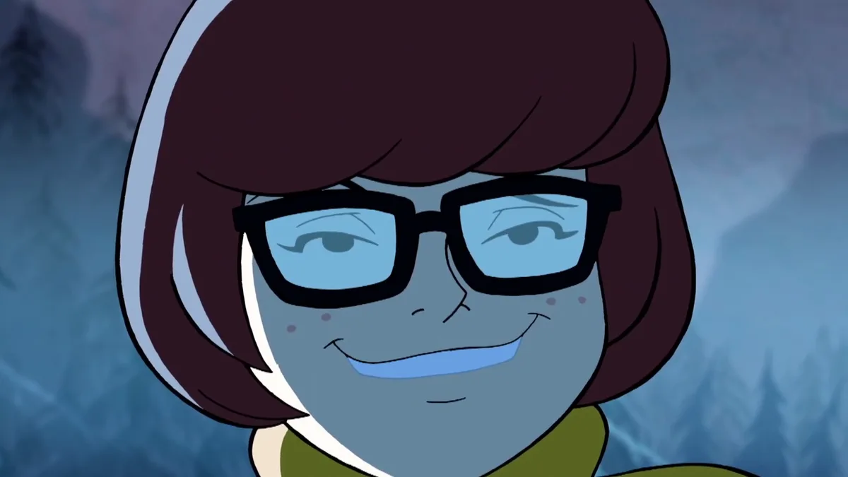 A close-up of the animated character Velma from Scooby-Doo, with her signature dark brown bob haircut, black-rimmed glasses…