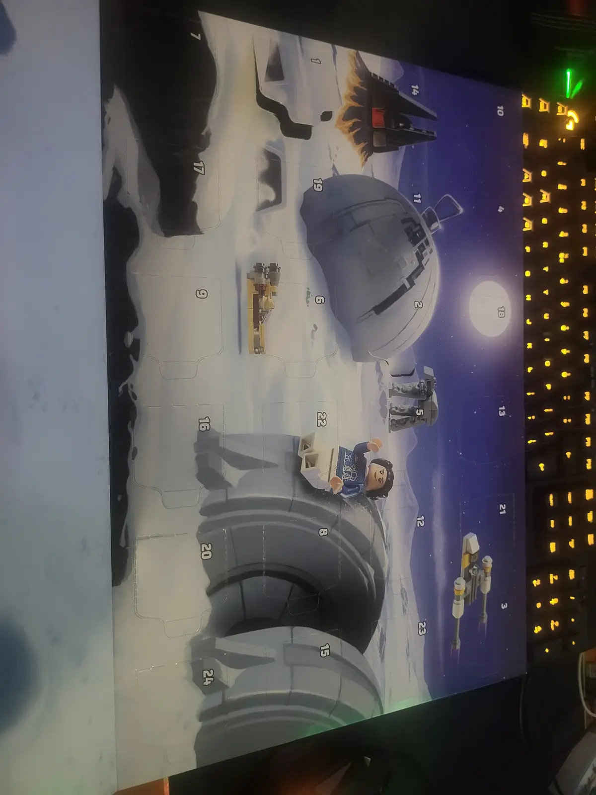 A close-up photo shows a partially opened LEGO Star Wars Advent Calendar, with numbered compartments revealing various Star…