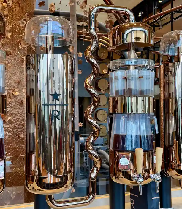 A photo of a Starbucks Reserve coffee setup with shiny copper and glass equipment, including a large cylindrical tank with a…