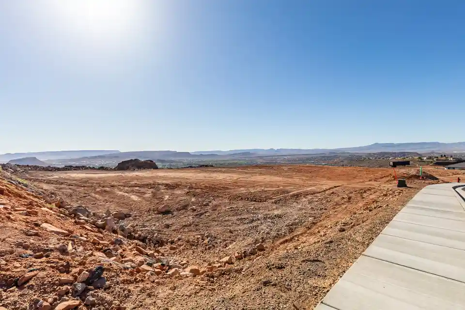 A wide-angle photo shows a vast, barren desert landscape with reddish-brown dirt, scattered rocks, and distant mountains…