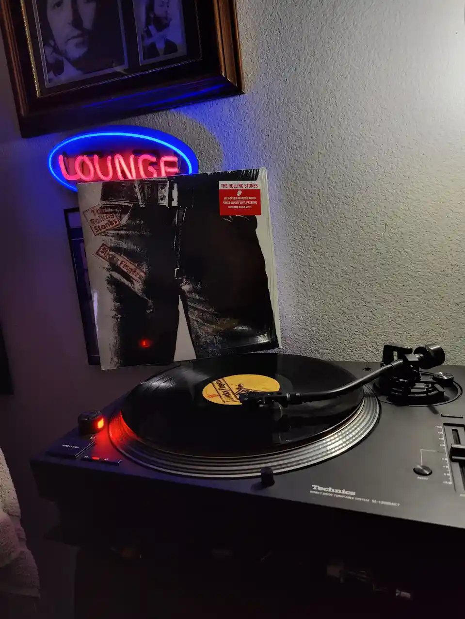 A Technics turntable plays a vinyl record, with the album cover for The Rolling Stones' 'Sticky Fingers' propped up behind…