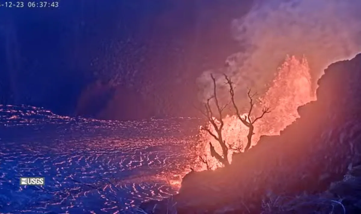 A dramatic nighttime volcanic eruption scene shows glowing orange lava flowing over a dark landscape, illuminated by the…